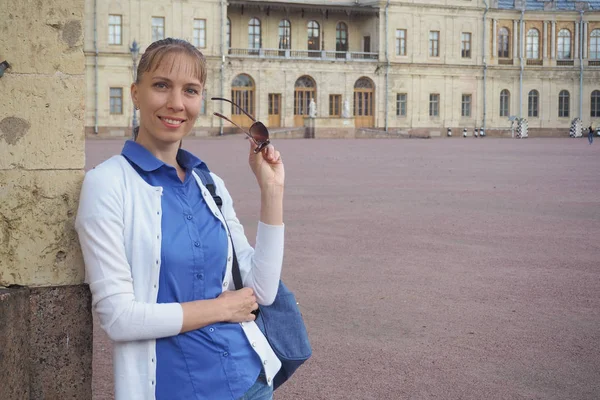 Uma mulher sorridente turista caminhando na cidade. Uma turista feminina na rua em frente à arquitetura antiga . — Fotografia de Stock