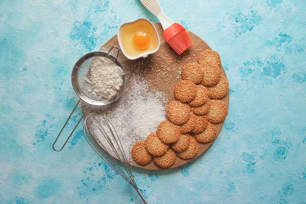 Κάτοψη του σύνολο προϊόντων για μαγείρεμα cookies, μαγειρικά σκεύη και αρκετές στρογγυλά μπισκότα με σουσάμι σε ένα μπλε ξύλινο τραπέζι. — Φωτογραφία Αρχείου