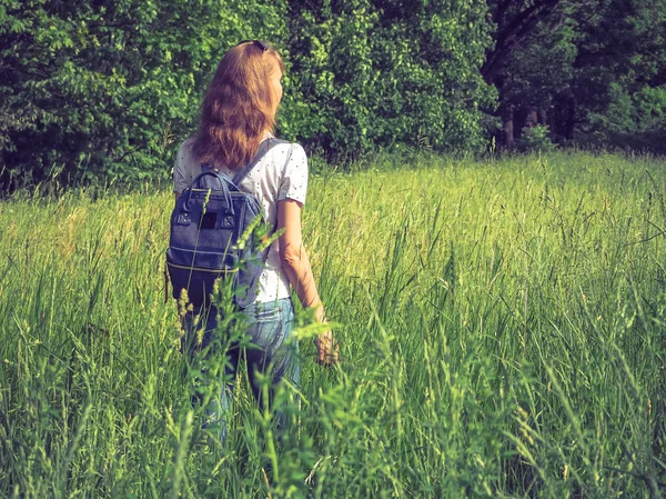 Bir sırt çantası ile ince bir kadın uzun boylu çimenlerin üzerinde seyahat.