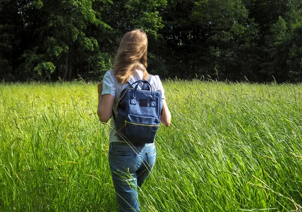 Bir sırt çantası ile ince bir kadın uzun boylu çimenlerin üzerinde seyahat.