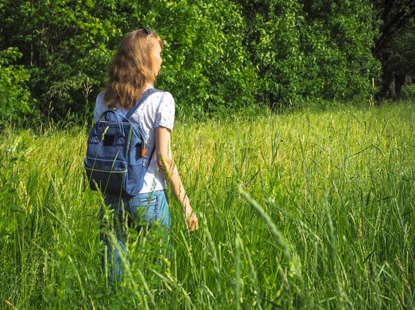 A slender woman with a backpack travels on the tall grass.
