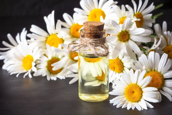 Botella de aceite de manzanilla con flores sobre fondo negro —  Fotos de Stock