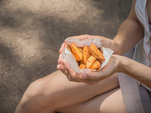 A girl holding a pack of fries in hand in the street. Small pack of potato fries, fast snack