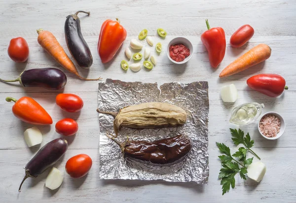 Баклажан, выпекаемый на фольге, и овощи выкладываются на деревянный стол. Овощи на светлом деревянном фоне . — стоковое фото