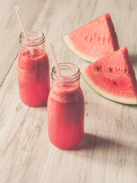 Jugo de sandía recién exprimido en botellas sobre una mesa de madera blanca —  Fotos de Stock