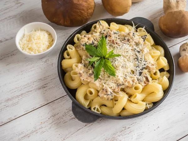 Makarna ile dökme demir kuruş çörek tava üzerinde beyaz bir ahşap masa.