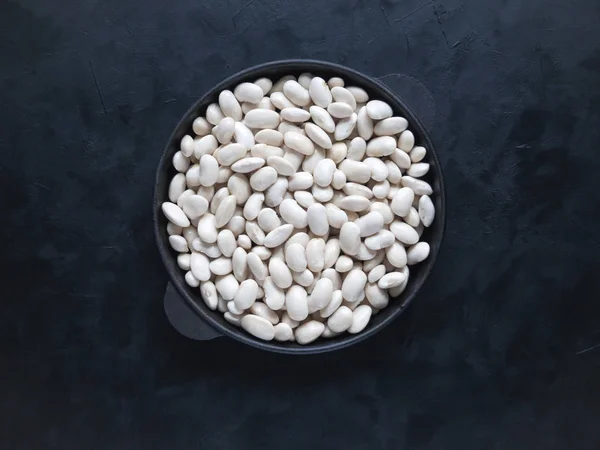 White beans in a frying pan on a black table.