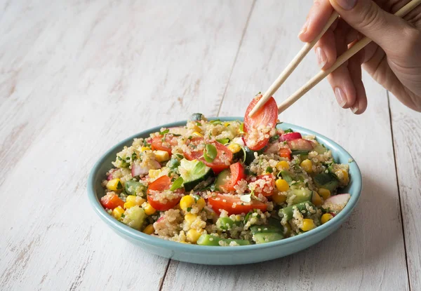 Chopsticks eat salad with quinoa. Close up.