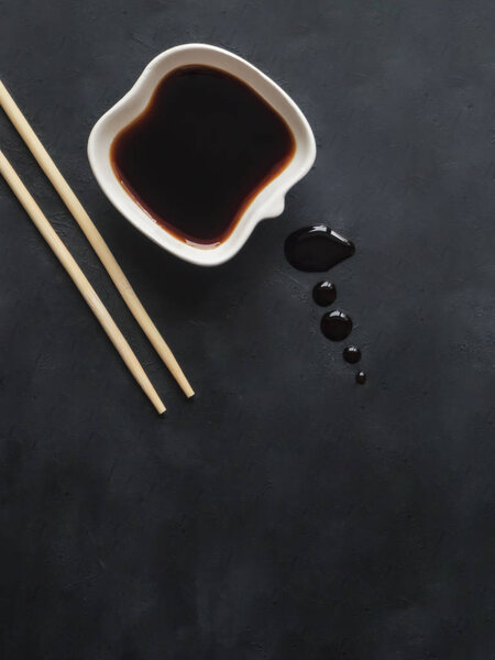 Chopsticks and soy sauce on black background.