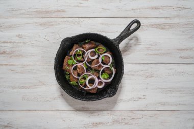 Dana eti parçaları üzerinde eski bir dökme demir tava ihtiva eder..