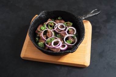 Eski bir siyah tavada sığır eti parçaları.