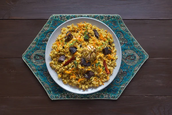 Pilaf uzbeko in un piatto su un tavolo di legno marrone . — Foto Stock
