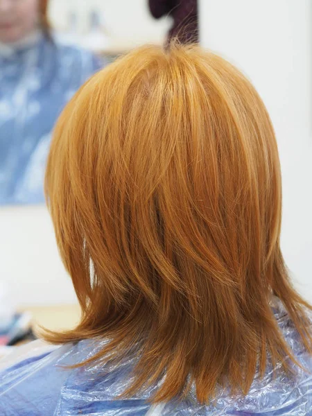 Red-haired girl back view in a hairdressing salon.