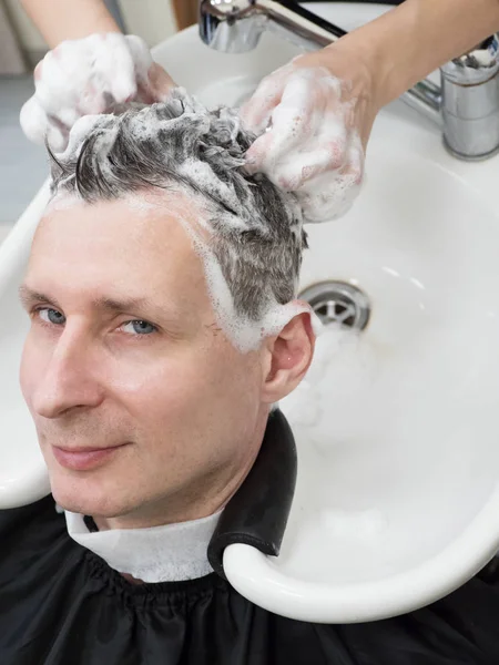 Un hombre se lava el pelo después de un corte de pelo . — Foto de Stock