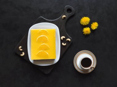 Portakallı sarı cheesecake ve siyah arka planda bir fincan kahve.