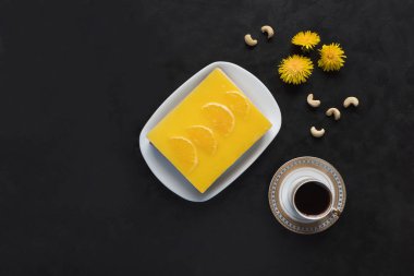 Portakallı sarı cheesecake ve siyah arka planda bir fincan kahve.