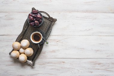 Beyaz ahşap masada tatlılar, hurma meyveleri ve kahve fincanı ile gümüş tabak üzerinde üst görünümü. Ramazan arka plan