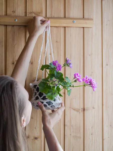 Mujer cuelga una maceta con una planta en maceta en la pared — Foto de Stock