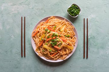 Yeşil bir masa üzerinde bir tabakta sebze ile Schezwan Noodles. Üst te. Hakka Noodles popüler bir Çin-Çin yemek tarifleri