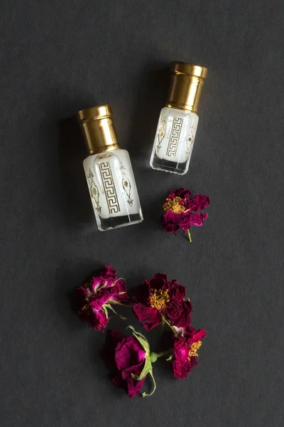 Skoncentrowane perfumy w mini butelce z kwiatowymi płatkami na czarnym stole — Zdjęcie stockowe