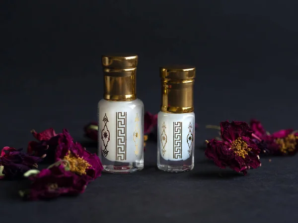 Skoncentrowane perfumy w mini butelce z kwiatowymi płatkami na czarnym stole — Zdjęcie stockowe