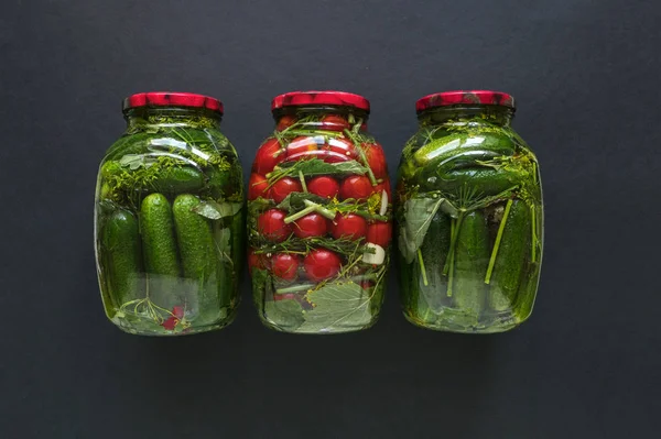 Latas de encurtidos y tomates para el invierno sobre fondo negro — Foto de Stock