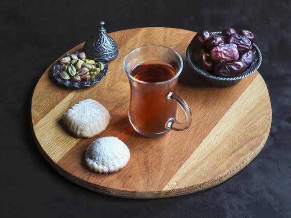 Teetasse mit ägyptischen Keksen "kahk el eid" und Datteln auf dem schwarzen Tisch — Stockfoto