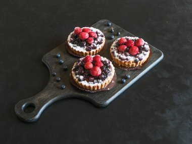 Üç lezzetli tart, siyah arka plan üzerinde taze ahududu ve yaban mersini ile renkli pasta kek tatlılar