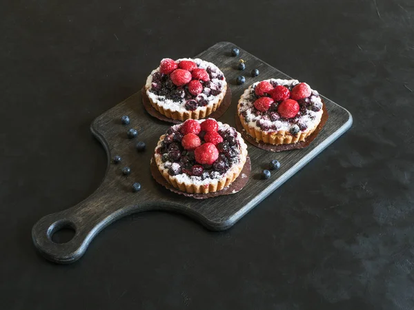 Three delicious tarts, colorful pastry cakes sweets with fresh raspberries and blueberry on black background — Stock Photo, Image