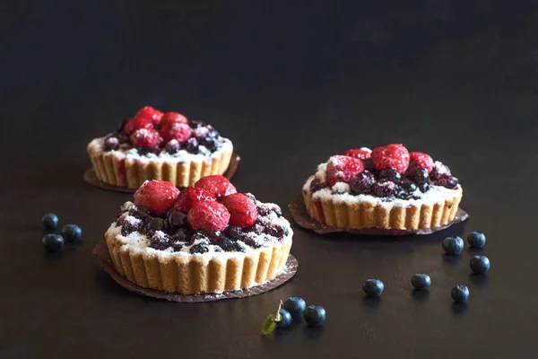Tres deliciosas tartas, pasteles de colores dulces con frambuesas frescas y arándanos sobre fondo negro — Foto de Stock