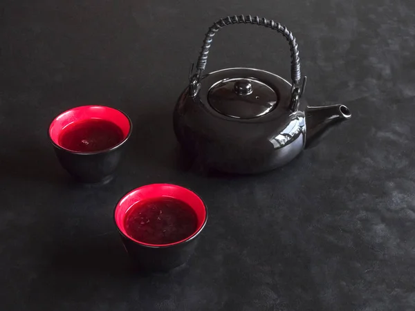 Zwei rote Tassen Tee und schwarze Teekanne auf schwarzem Tisch — Stockfoto