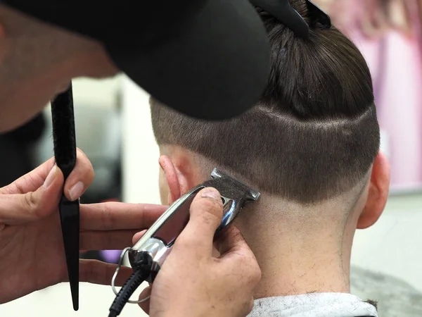 Peluquero con cortapelos trabaja en corte de pelo de barbudo chico barbería fondo — Foto de Stock