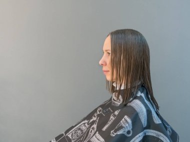 Kadının saçı gri bir duvarda kesiliyor..