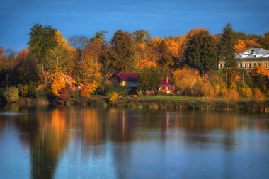 Aydınlık sonbahar manzarası yansımalı ve göl kenarındaki evler.