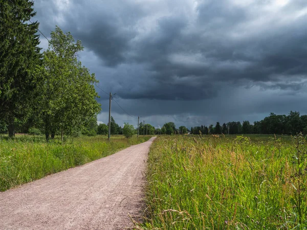 Droga przez zielone pole i chmury na ciemnym niebie w letni dzień — Zdjęcie stockowe