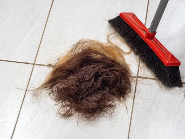 Uma pilha de cabelo cortado no chão da barbearia ao lado de uma vassoura — Fotografia de Stock