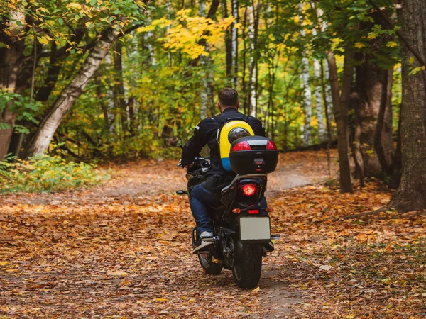 Motorradfahrerin fährt mit Hund im Rucksack auf dem Rücken auf Waldweg. — Stockfoto