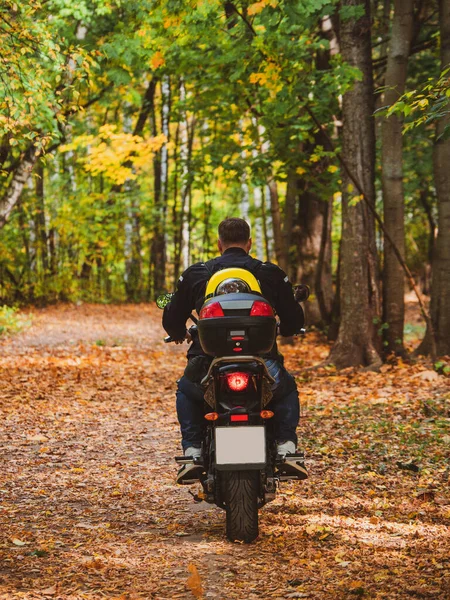 Biker on a motorcycle rides along a forest road with a dog in a backpack on his back