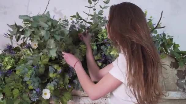 Floristin steht in luftiger Höhe mit Eukalyptuszweigen in der Hand und schmückt Blumen an schönen Holztoren — Stockvideo