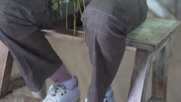 La cámara se mueve hacia arriba: una chica con los ojos cerrados y una rama de vegetación se sienta en una escalera de madera — Vídeos de Stock