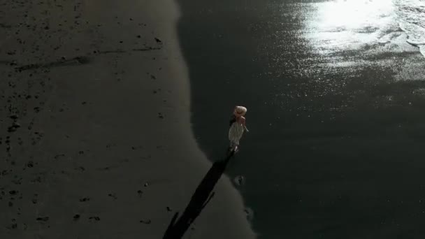 Veduta aerea - una donna in abito lungo e cappello corre lungo la spiaggia di sabbia nera a Los Gigantes, Tenerife, Isole Canarie, Spagna — Video Stock