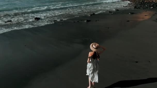 Die schönste Luftaufnahme: ein Mädchen mit Hut und Kleid läuft am schwarzen Strand entlang, danach ein Blick auf die los gigantes, Teneriffa, Kanarische Inseln, Spanien — Stockvideo