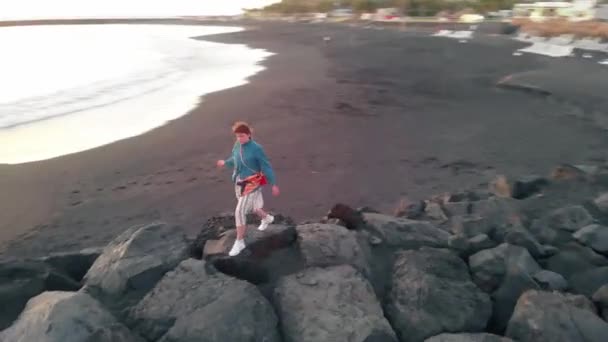 Жінка стоїть на узбережжі Атлантичного океану, камера рухається навколо неї, вид з безпілотника — стокове відео