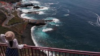 Havadan görüntüleri - bir şapka şık ve modern kız Atlantik Okyanusu'nda bir adanın kıyısında bir uçurumun kenarında duruyor