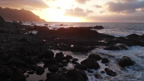 Letecké. Pláž při západu slunce. Výhled se otevírá na černé kameny a sopečný písek, zlatou hodinu. Kamera se pohybuje kupředu. Pohled z dronu. Tenerife, Kanárské ostrovy, Španělsko — Stock video