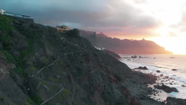 Luchtfoto van de lange kustlijn bij zonsondergang: de kliffen en de Atlantische Oceaan, stranden met zwart vulkanisch zand en kleurrijke kleine steden, Tenerife, Spanje — Stockvideo