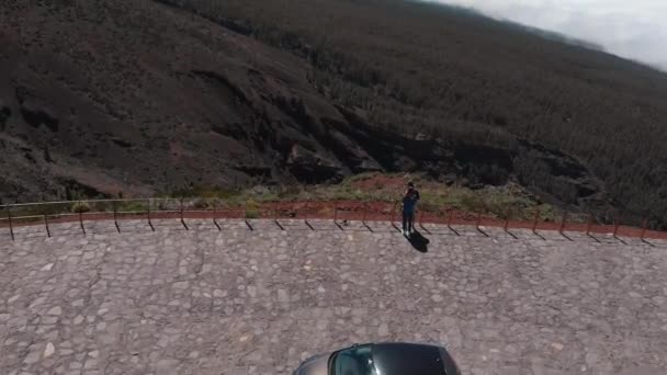 Aerial view - a young couple stands on the edge of the observation deck. The view opens to the Teide volcano and the valley covered with dense forest and clouds. Martian landscape. — Stock Video