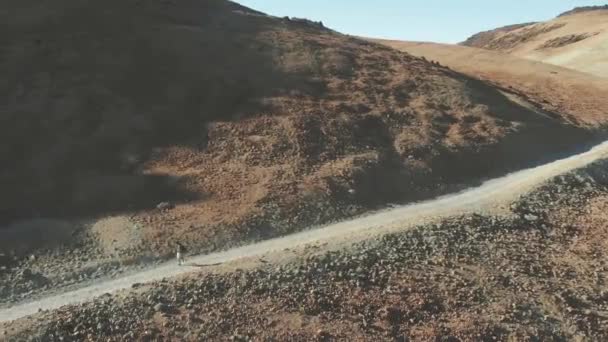 Εναέρια. Ένας χίπστερ περπατάει με ένα σακίδιο κατά μήκος ενός μονοπατιού στη βάση ενός ηφαιστείου, μέσω κατεψυγμένης λάβας και ηφαιστειακής άμμου. Τενερίφη, εθνικό πάρκο Teide. — Αρχείο Βίντεο