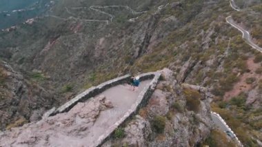Hava. Bir erkek ve bir kadın, dağların yükseklerinde bulunan bir izleme platformunun tam kenarında duruyorlar. Bulutlu hava, vadinin panoramik manzarası.