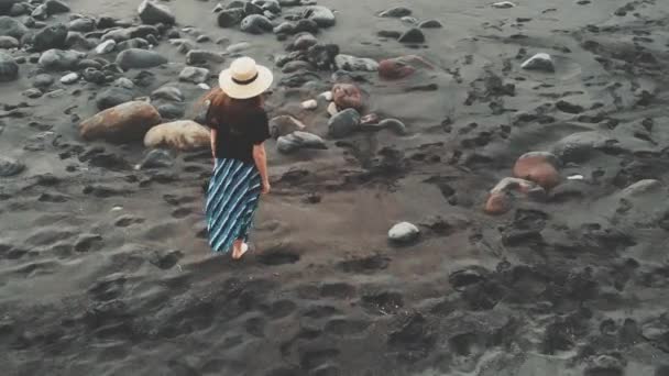 Des images aériennes parfaites de l "île de Ténérife - une jeune fille élégamment vêtue d'un chapeau, marchant le long d'une plage noire de sable volcanique. Vue panoramique cinématographique. Îles Canaries, Espagne — Video